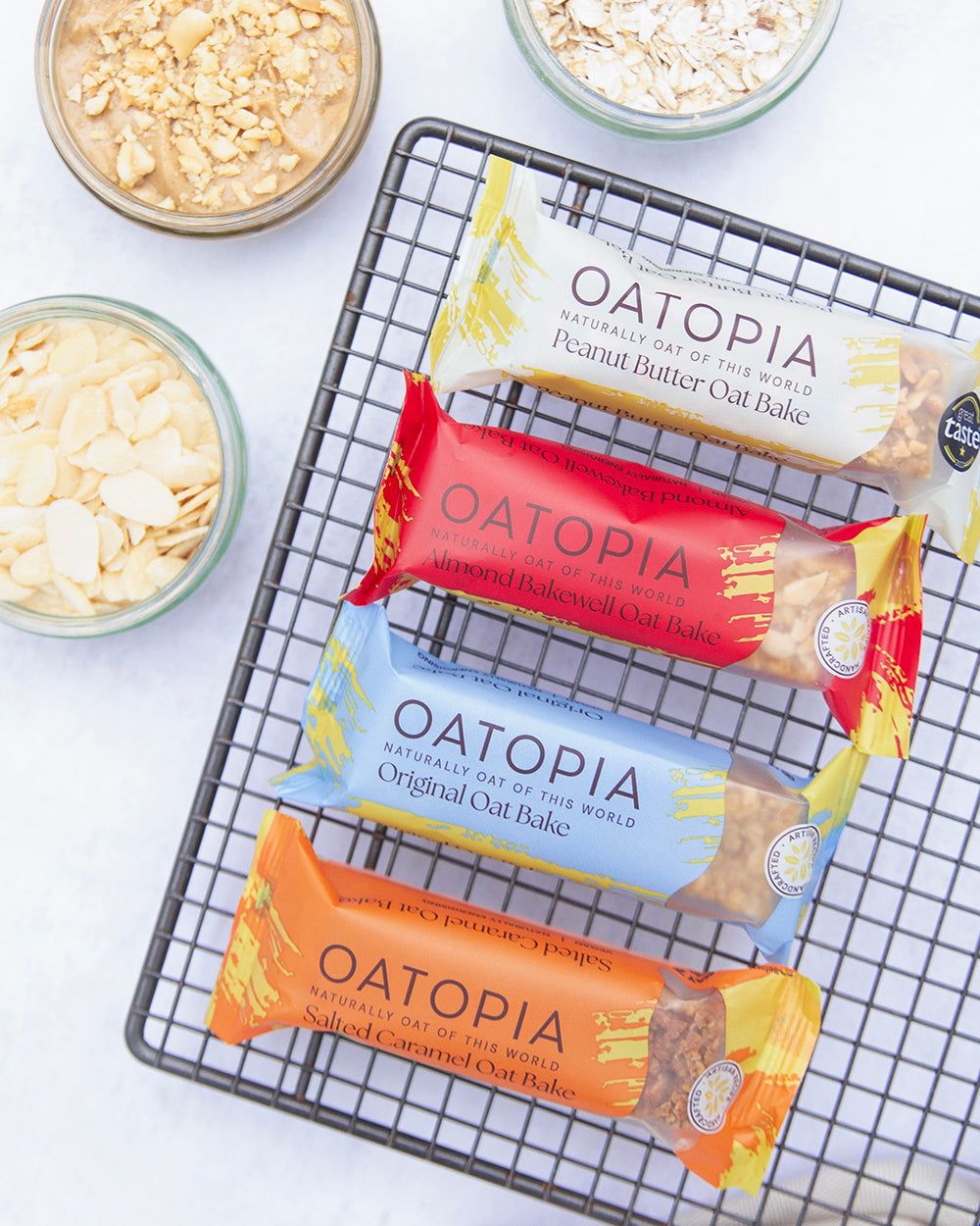 Oatopia snack-size oat bakes in colorful packaging on wire rack with ingredient bowls