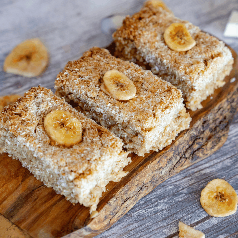 A wooden cutting board displaying golden banana and coconut flapjacks, showcasing their tropical flavor and soft texture.