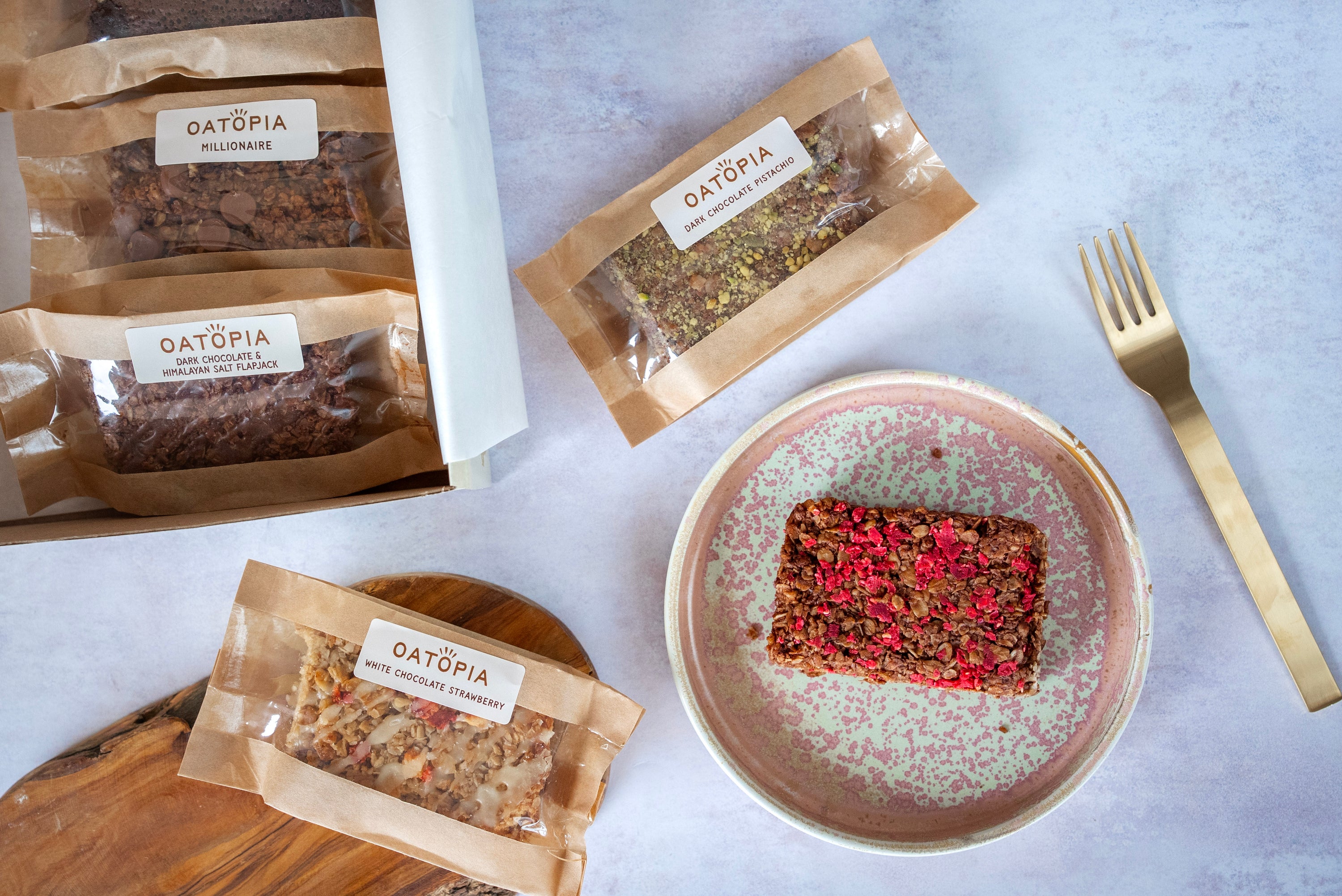 Oatpia flapjack bars on a plate with packaging and a fork on a light background