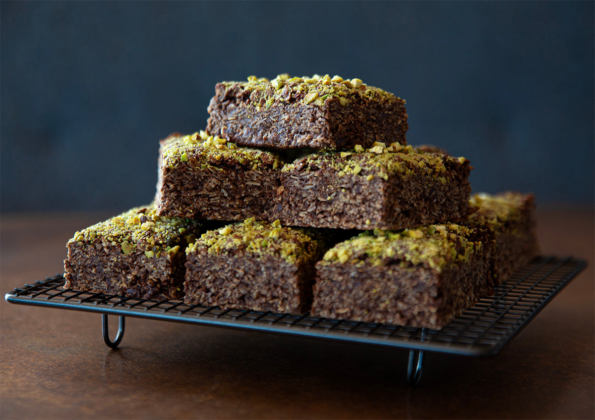 Stack of brownies with green crumb topping on a cooling rack against a dark background