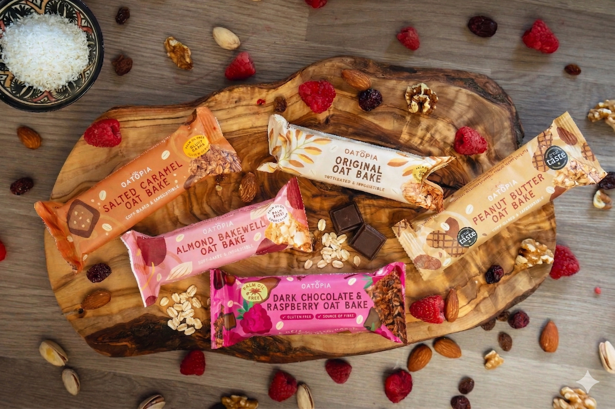 Five flavors of Oatopia oatbake bars on a wooden slab with nuts, oats and fruits scattered all around.
