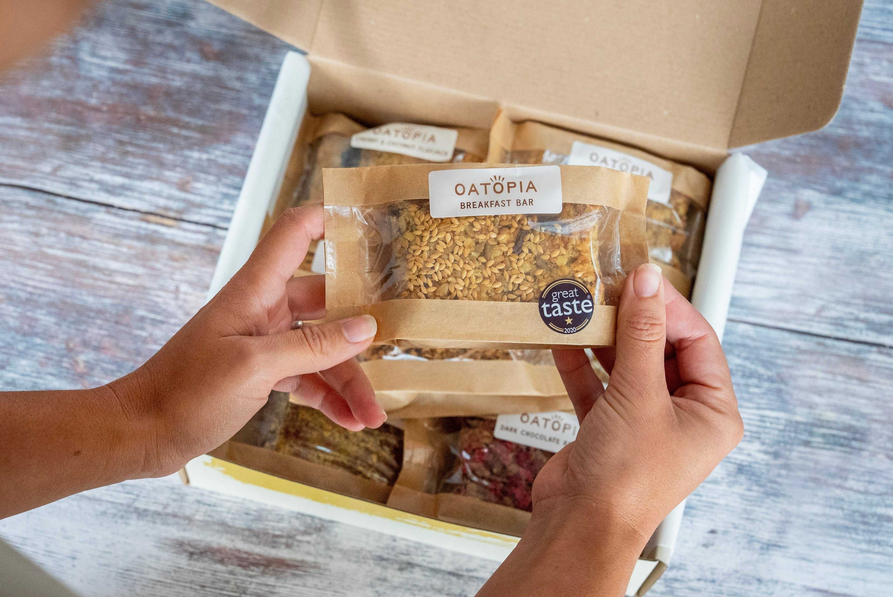 Founder's Favourite vegan flapjack box with assorted oat bars including breakfast bar, held over open package on wooden surface