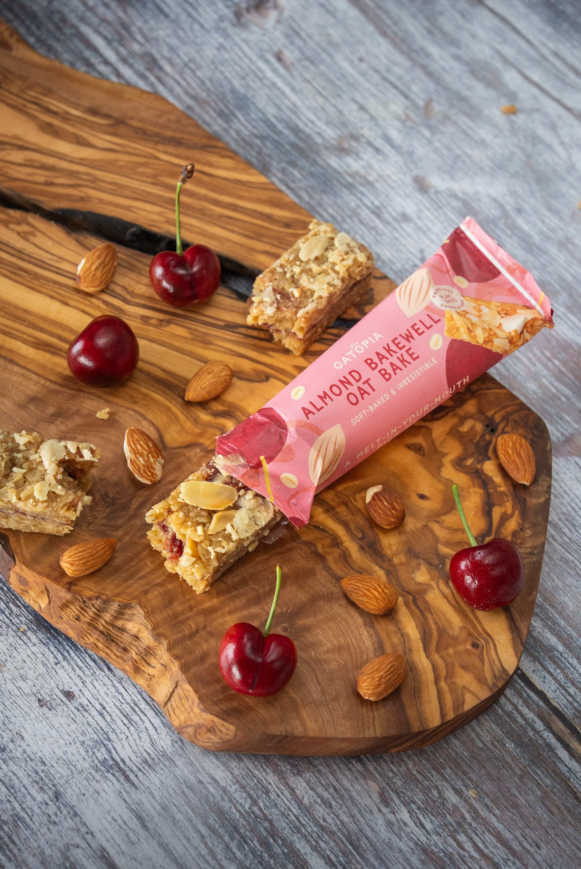 Oatopia Almond Bakewell Oat bake 60 on a wooden slab wit nuts and fruits around
