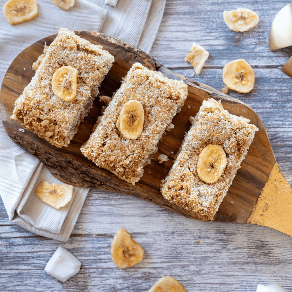  Close-up of banana and coconut flapjacks on a wooden cutting board, highlighting their rich caramelized finish and toasted coconut.
