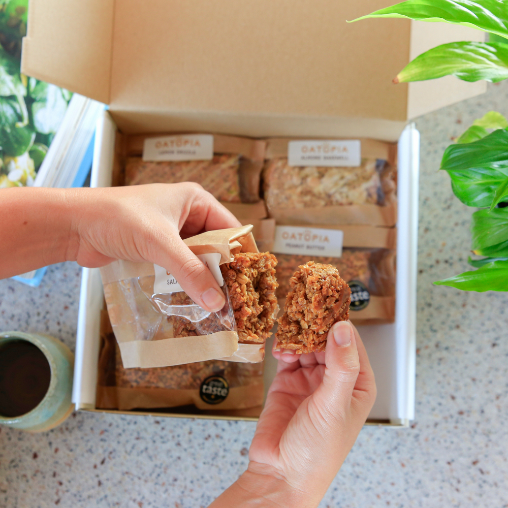 Hands breaking open a soft-baked Oatopia Salted Caramel flapjack above the Best Seller gift box.