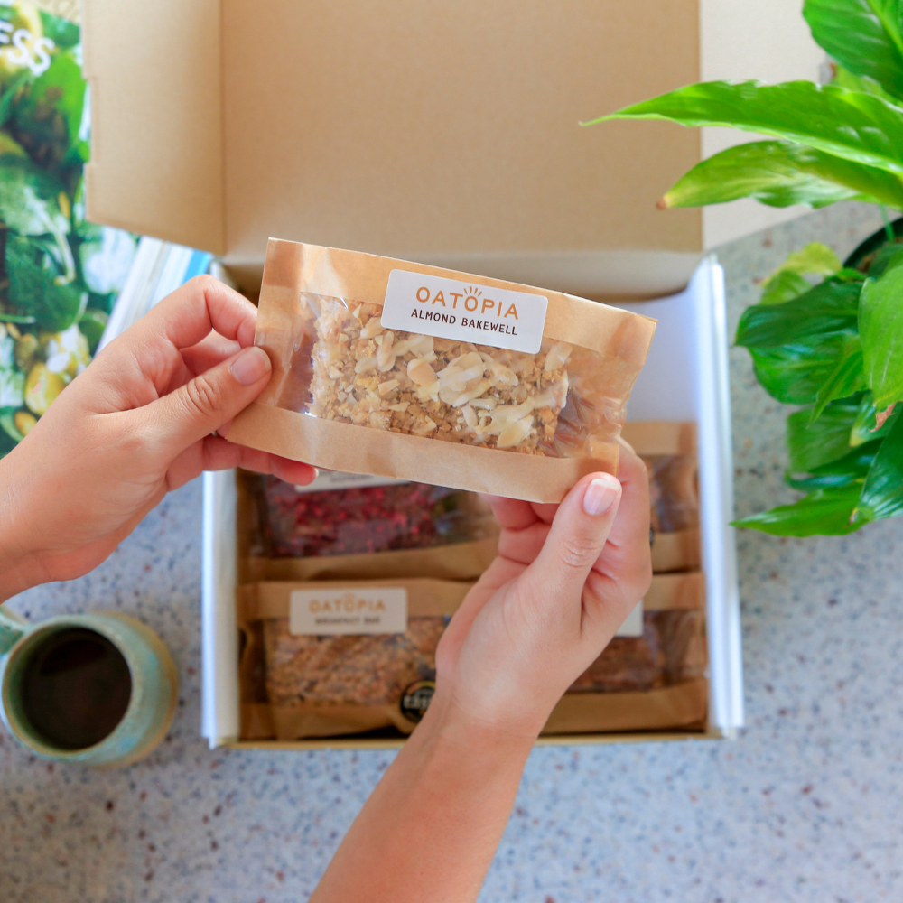 Close-up of an individually wrapped Oatopia Almond Bakewell flapjack held above the Best Seller gift box.