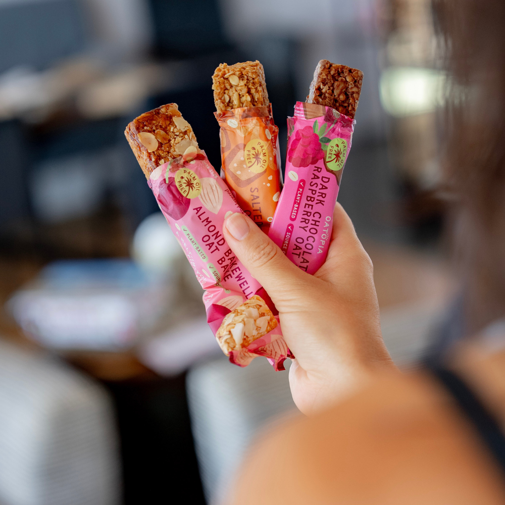 Three wrapped Oatopia Oat Bakes in Almond Bakewell, Salted Caramel and Dark Chocolate & Raspberry flavours.