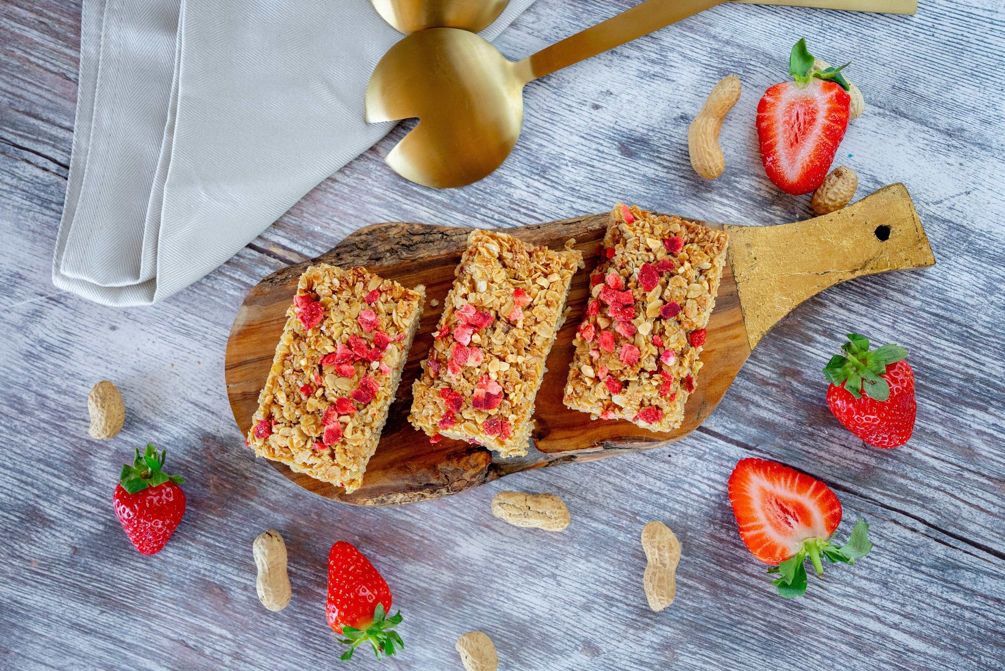 Three flapjack bars on a wooden board with strawberries and peanuts on a wooden surface.
