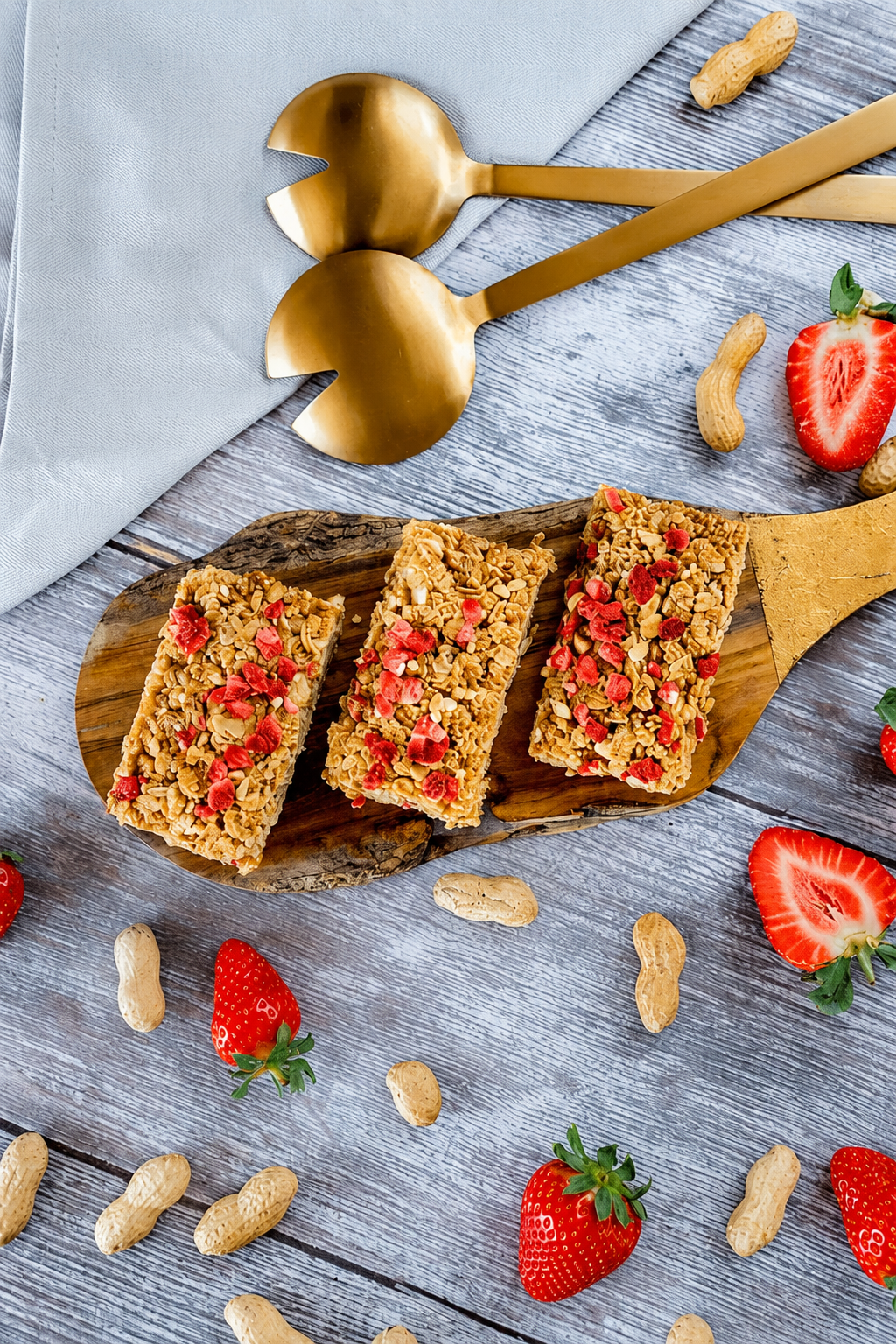A plate holds three peanut butter and jam flapjacks next to a wooden spoon and a bowl of ripe strawberries.