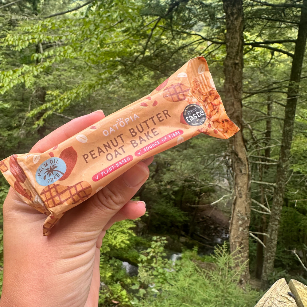 Oatopia Peanut Butter Oat Bake held outdoors against a green woodland background.