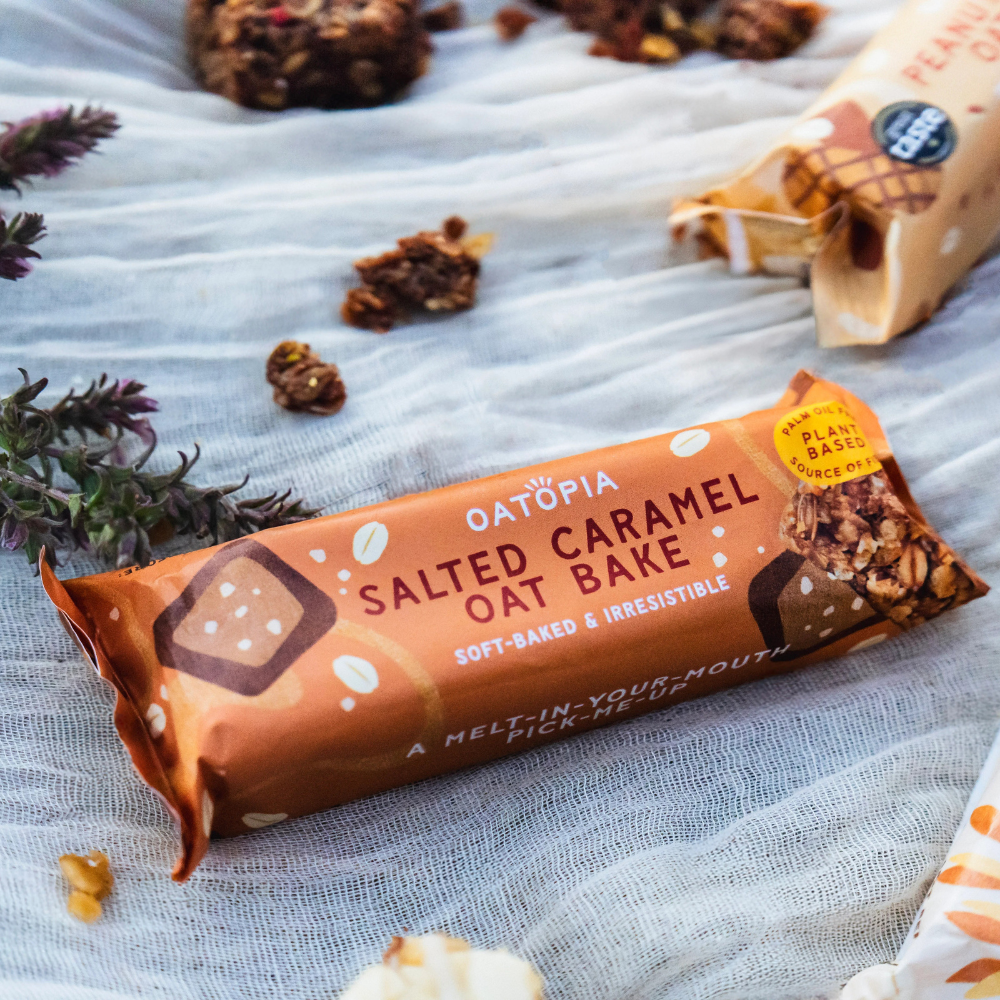 Wrapped Oatopia Salted Caramel Oat Bake styled on fabric with oats and dried flowers.
