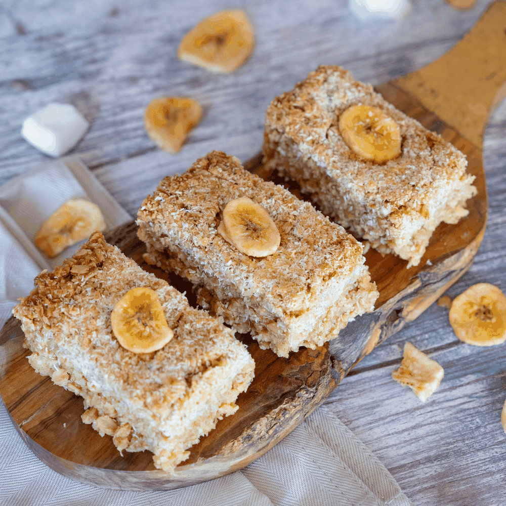 Close-up of banana and coconut flapjacks on a wooden cutting board, highlighting their rich caramelized finish and toasted coconut.