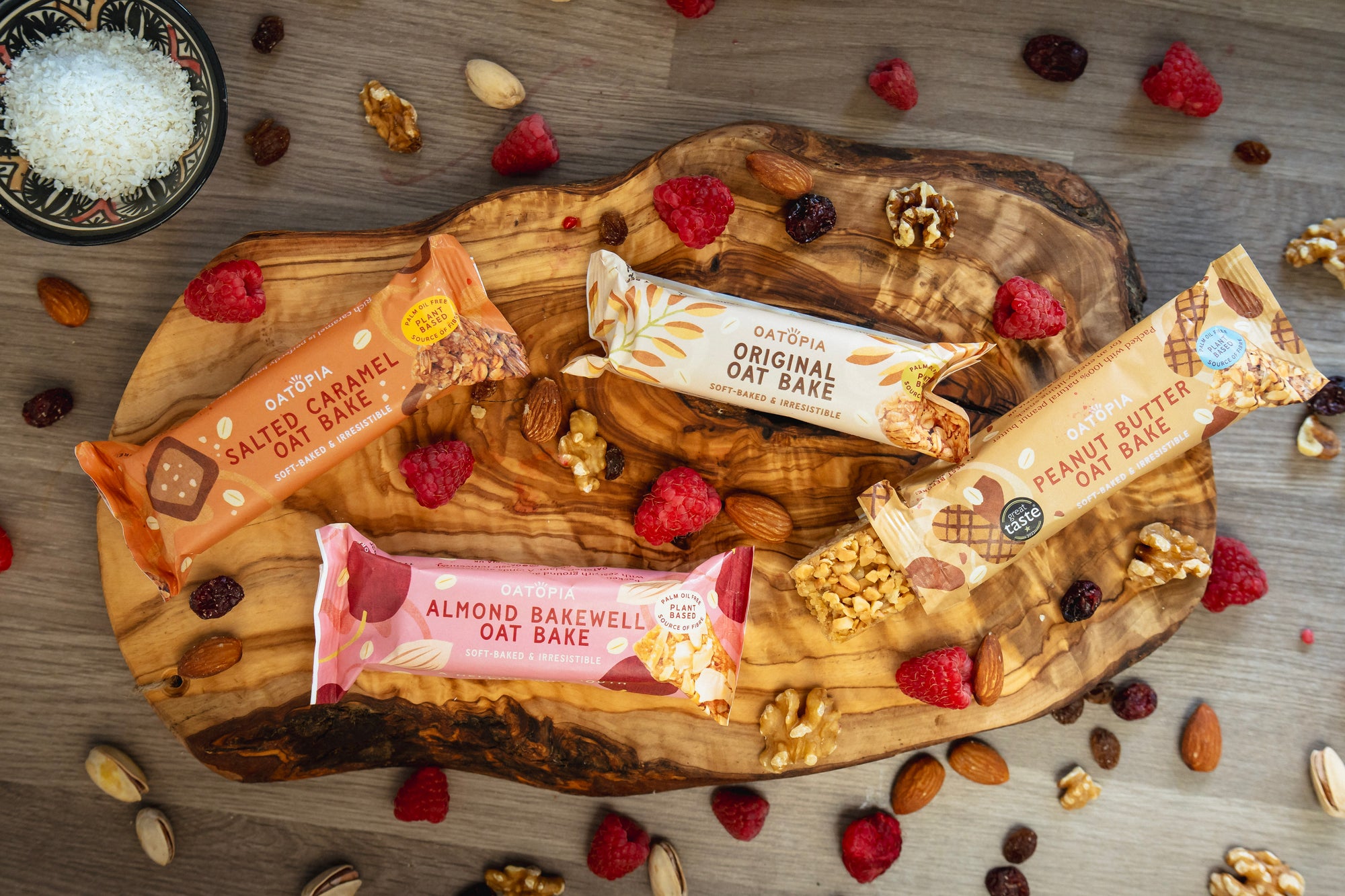 Oatopia Oat Bake bars on a wooden board with berries and nuts.