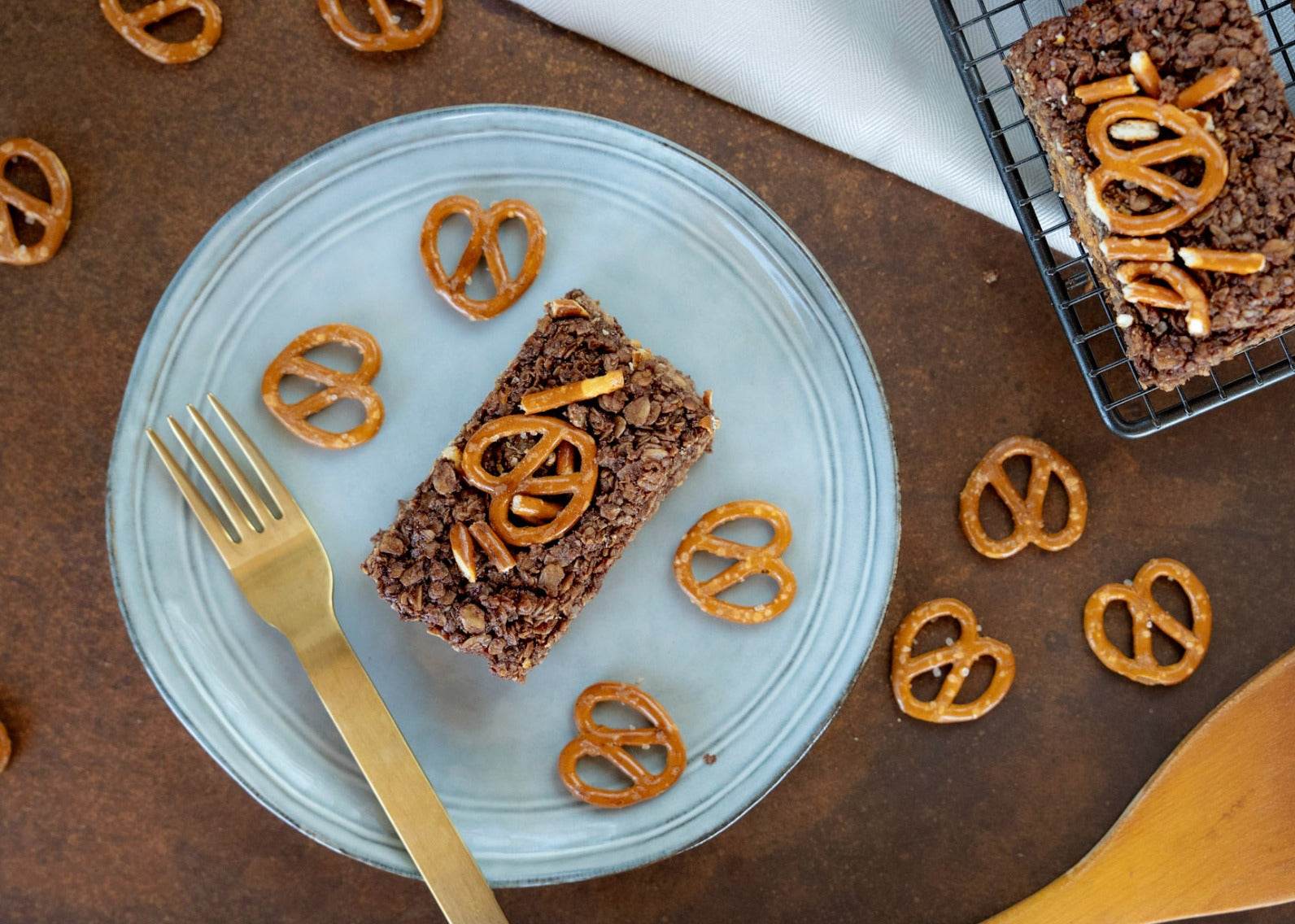 A piece of chocolate flapjack on a plate, adorned with pretzels and a creamy peanut butter topping.