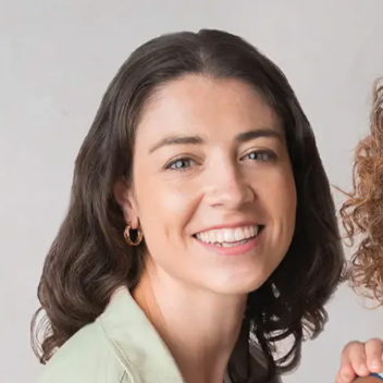 Woman in early adulthood with shoulder-length brown hair smiling against a plain background