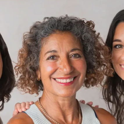 A middle aged woman with short, black and curly smiling against a neutral background. 