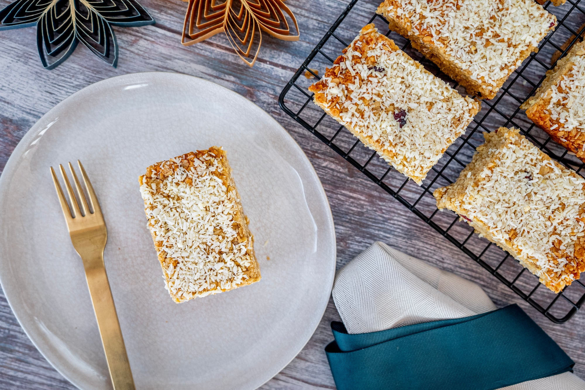 Square of cake on a white plate with a gold fork, surrounded by more cakes on a cooling rack.