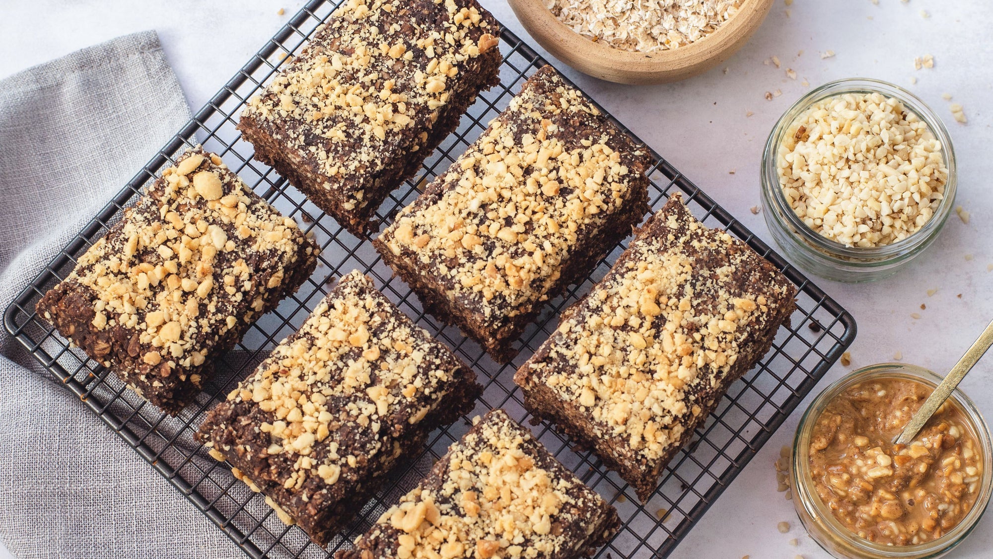 Brownies on a cooling rack with oats and peanut butter jars on a light background