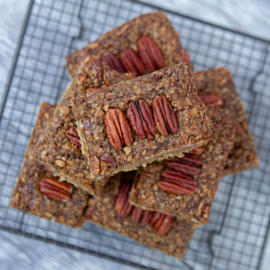 Stack of flapjacks with visible pecan nuts on top, cooling on a wire rack.