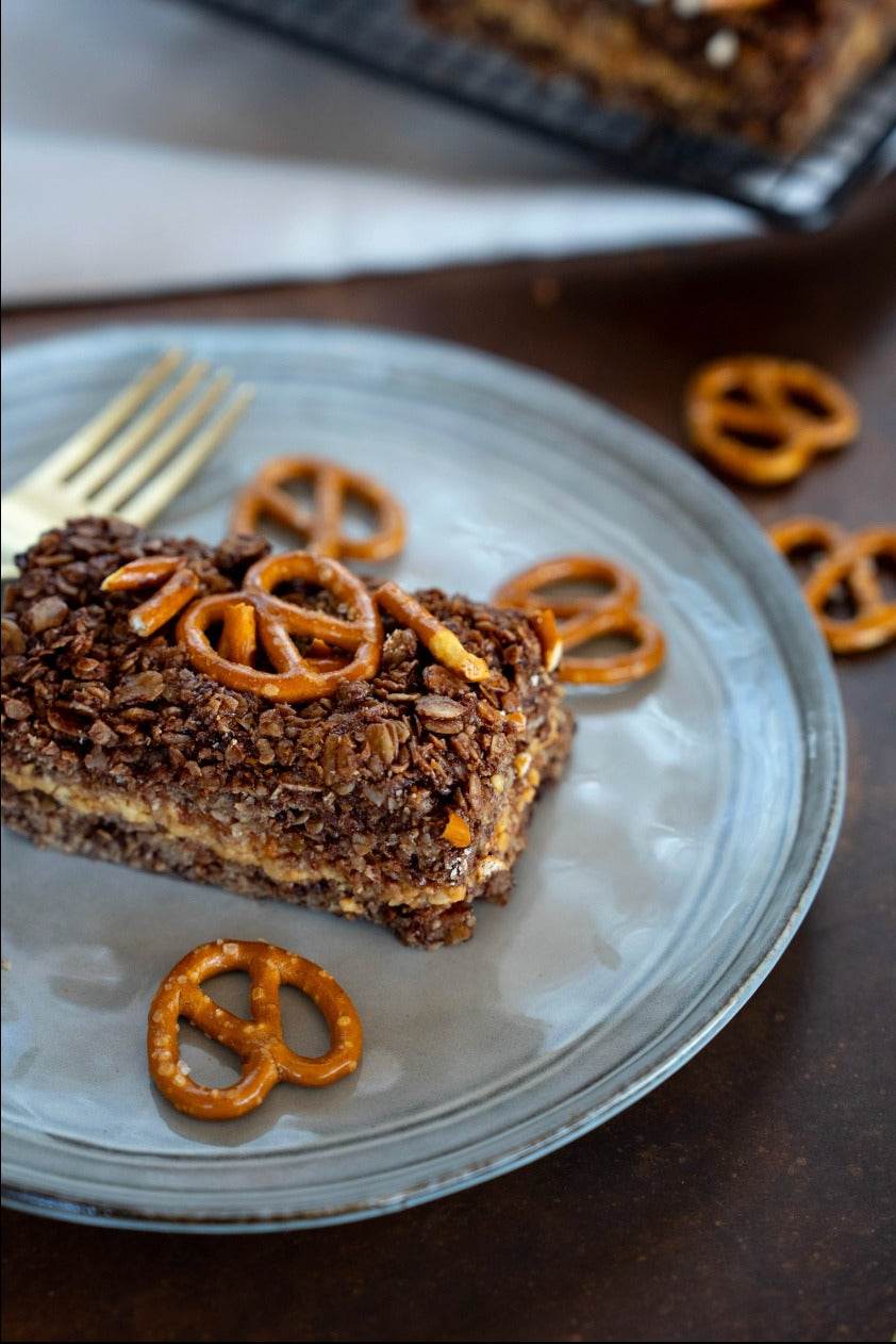 Salted pretzel topped vegan peanut butter chocolate flapjack with crunchy pieces and rich layers