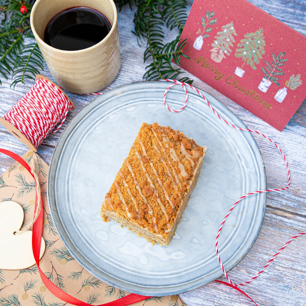  A thick slice of gingerbread-inspired cake on a plate next to a cup of coffee, embodying festive flavors and comfort.