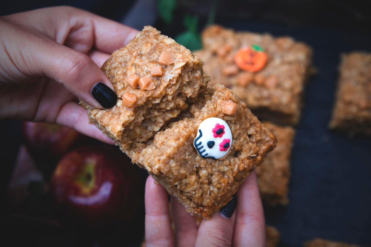 A person holds two Halloween-themed oatmeal bars, decorated with spooky designs and vibrant colors.